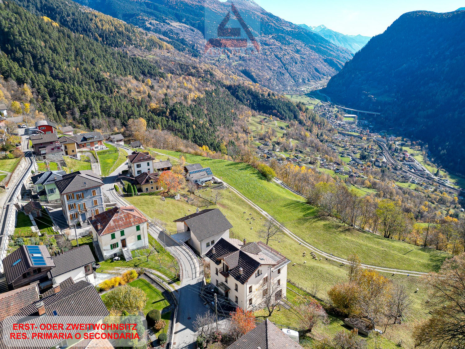 Mountain village with several houses, green fields, and a valley in the background
