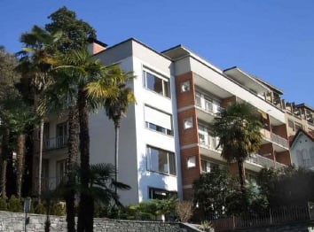 Multi-story apartment building with balconies, surrounded by palm trees and greenery