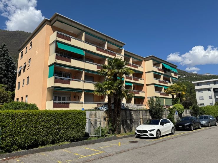 multi-story building, beige exterior, green awnings, balconies, hedges, palm tree, cars parked