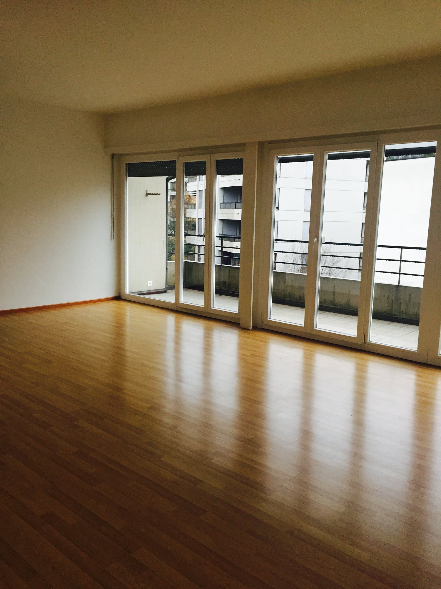 large empty room with wooden floor, sliding doors leading to balcony, white walls