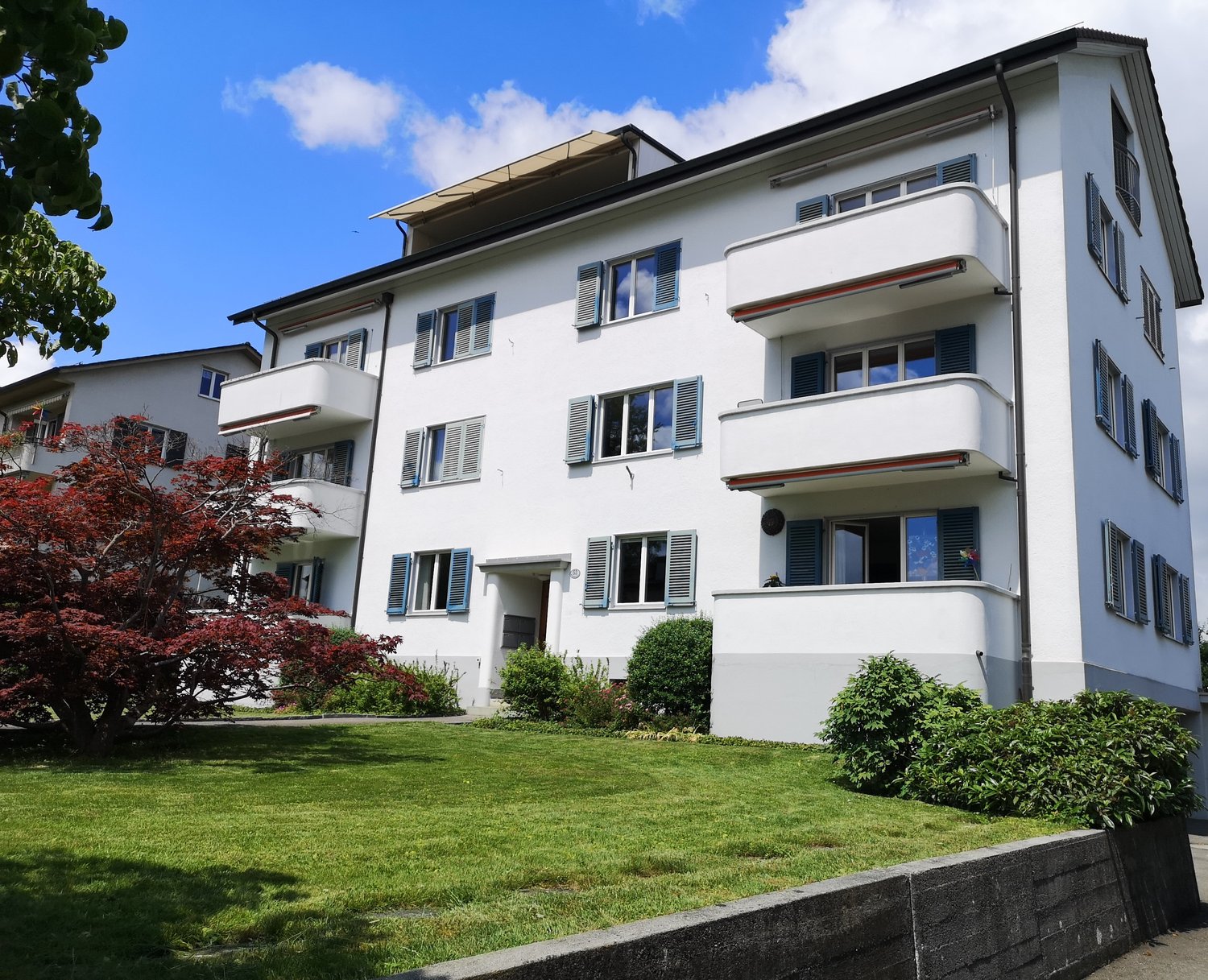 4-story apartment building, white exterior, multiple balconies, red foliage tree