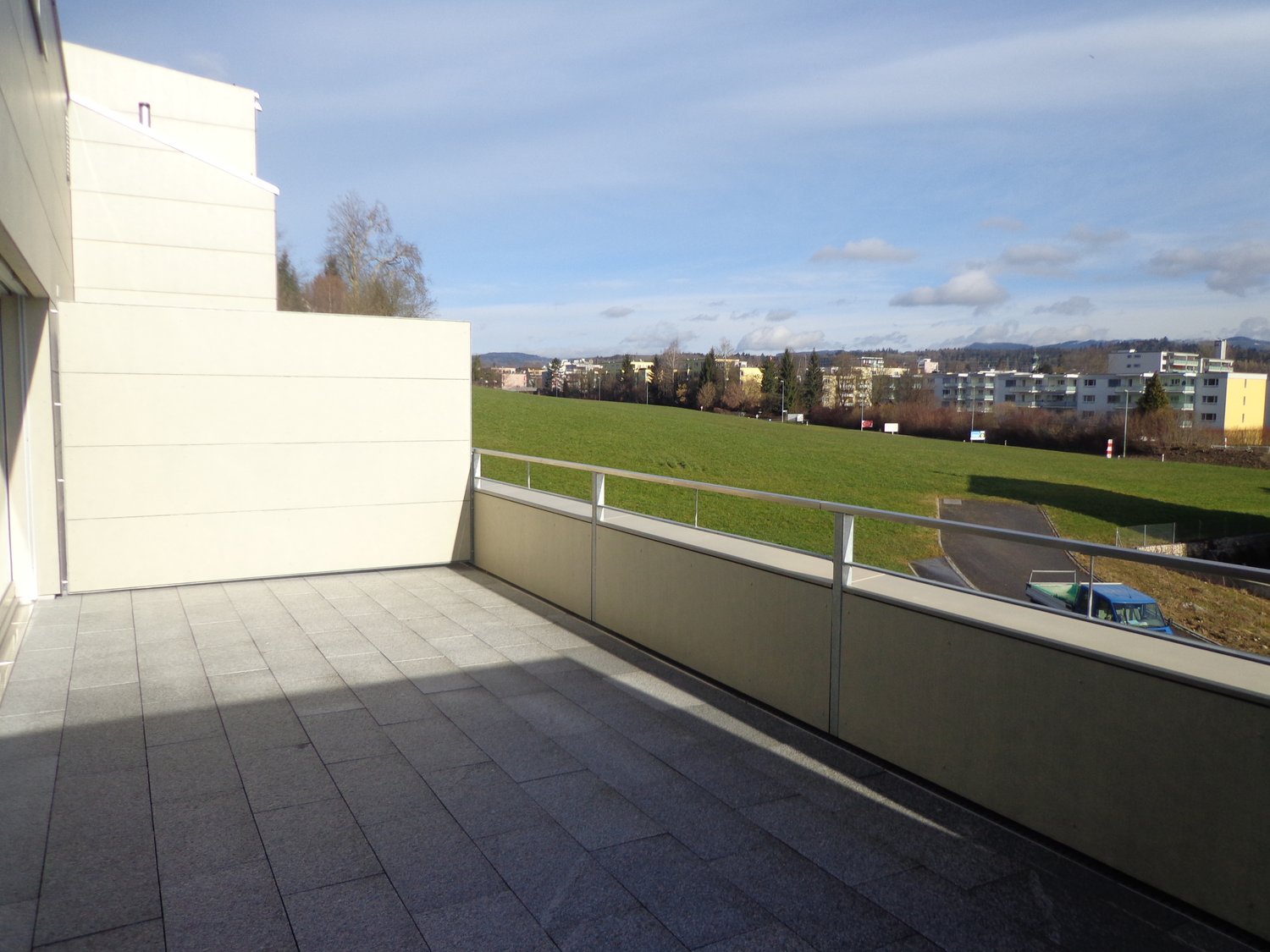 Balcony with a panoramic view over a grassy field and city skyline in the distance, featuring a modern metal railing