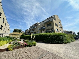 residential apartment building, multiple floors, balconies, driveway, well-maintained landscaping, greenery, multiple cars parked in designated parking area