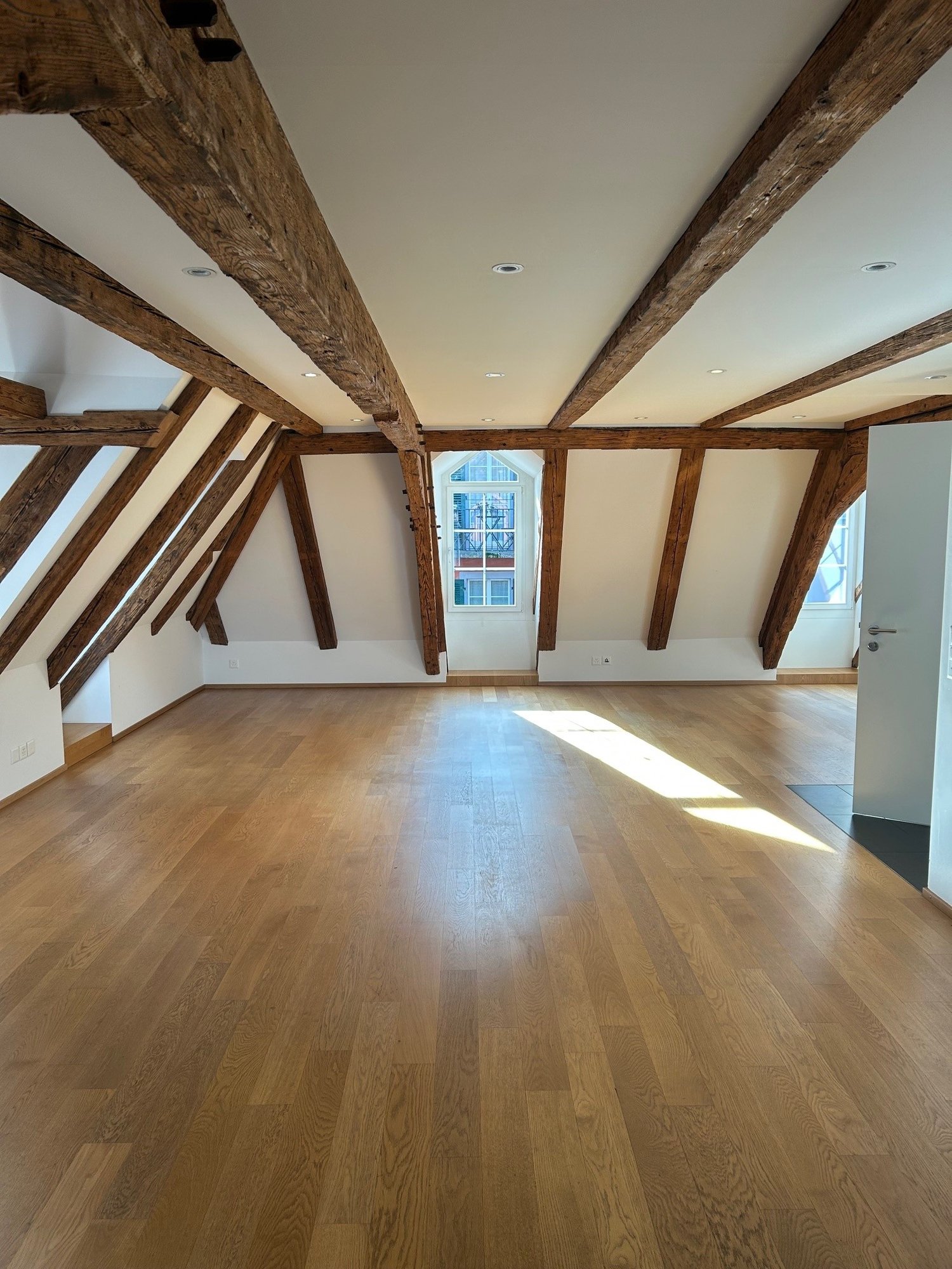 Large attic room with wooden beams, wooden flooring, and a skylight window.