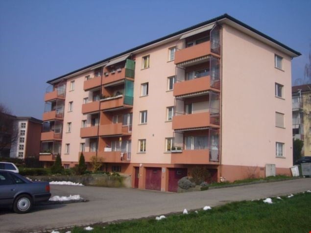 4-story apartment building with orange and beige exterior, balconies on each unit, and a parking area in front