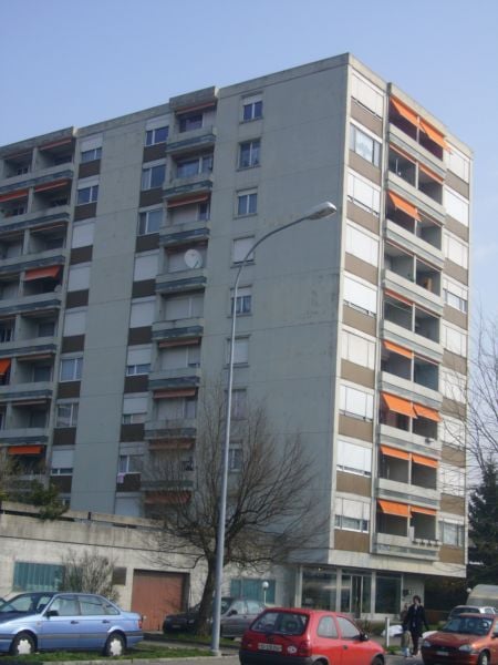 multistory residential building, many balconies, gray facade, orange awnings