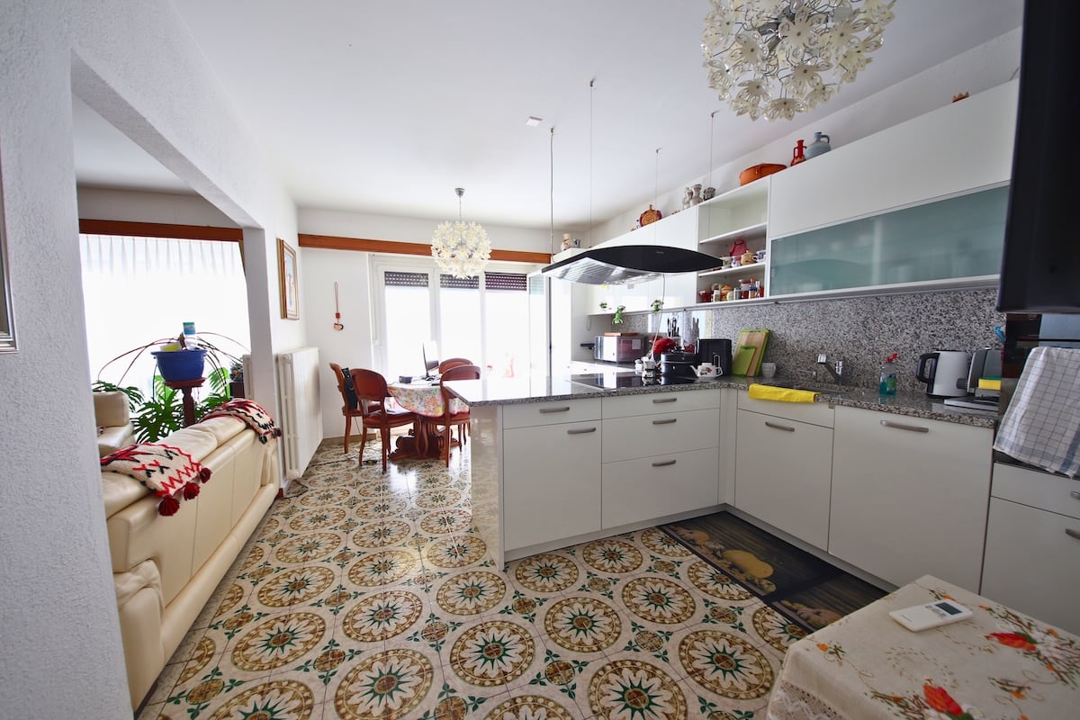 white kitchen, dining room with table and chairs, couch with decorative blanket, potted plant, large windows, modern flooring