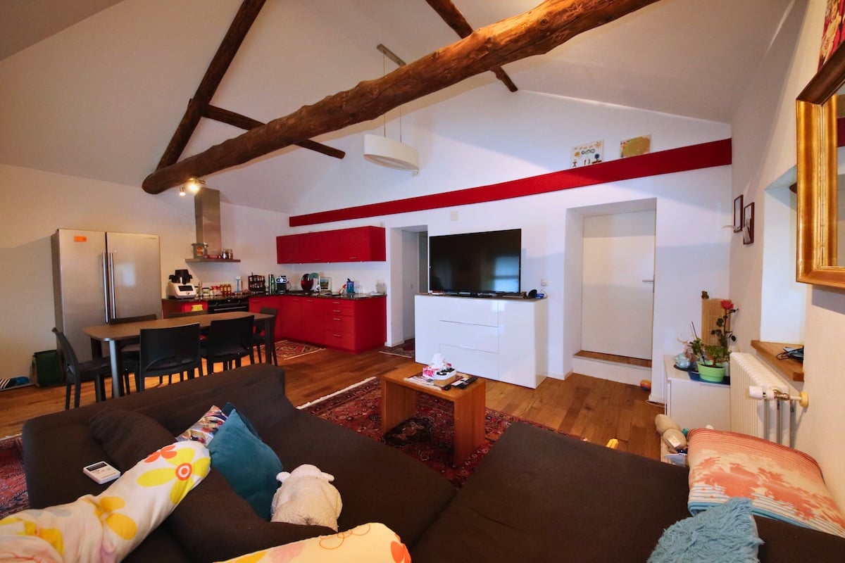 modern furnishings, exposed wooden beams, refrigerator, TV on cabinet, wooden table and chairs, red cabinets, open floor plan