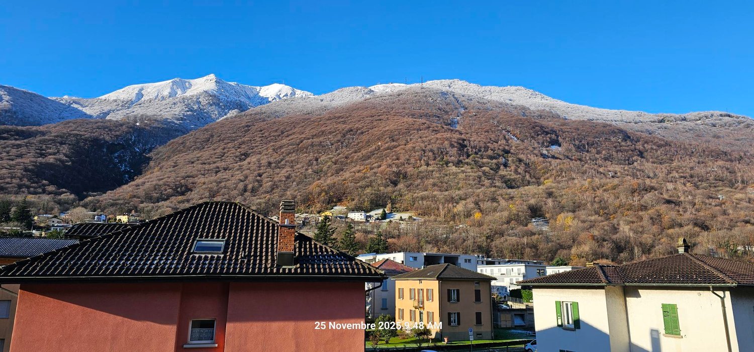 Building with tiled roof, neighboring houses, snowy mountains, clear sky