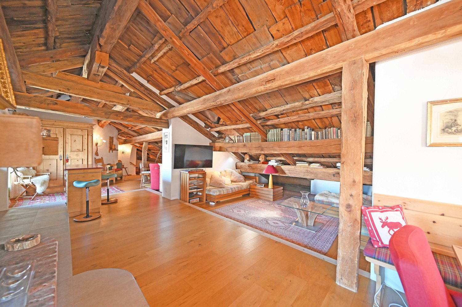 Spacious living room with exposed wooden beams and ceiling, hardwood floors, built-in bookshelves, sofa, coffee table, and a fireplace