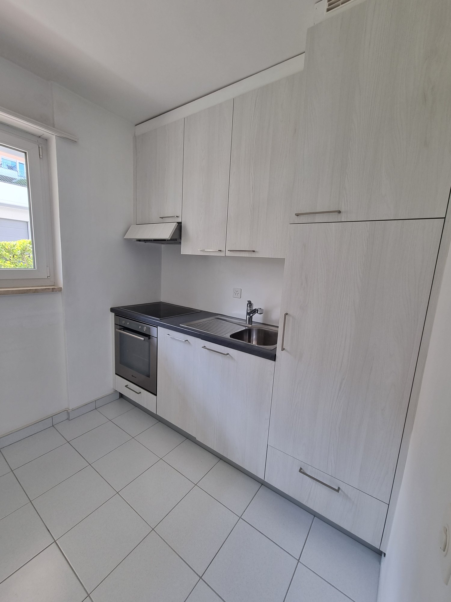 modern kitchen with white tiles, white cabinets, black countertops, electric oven, stainless steel sink, faucet, extractor hood