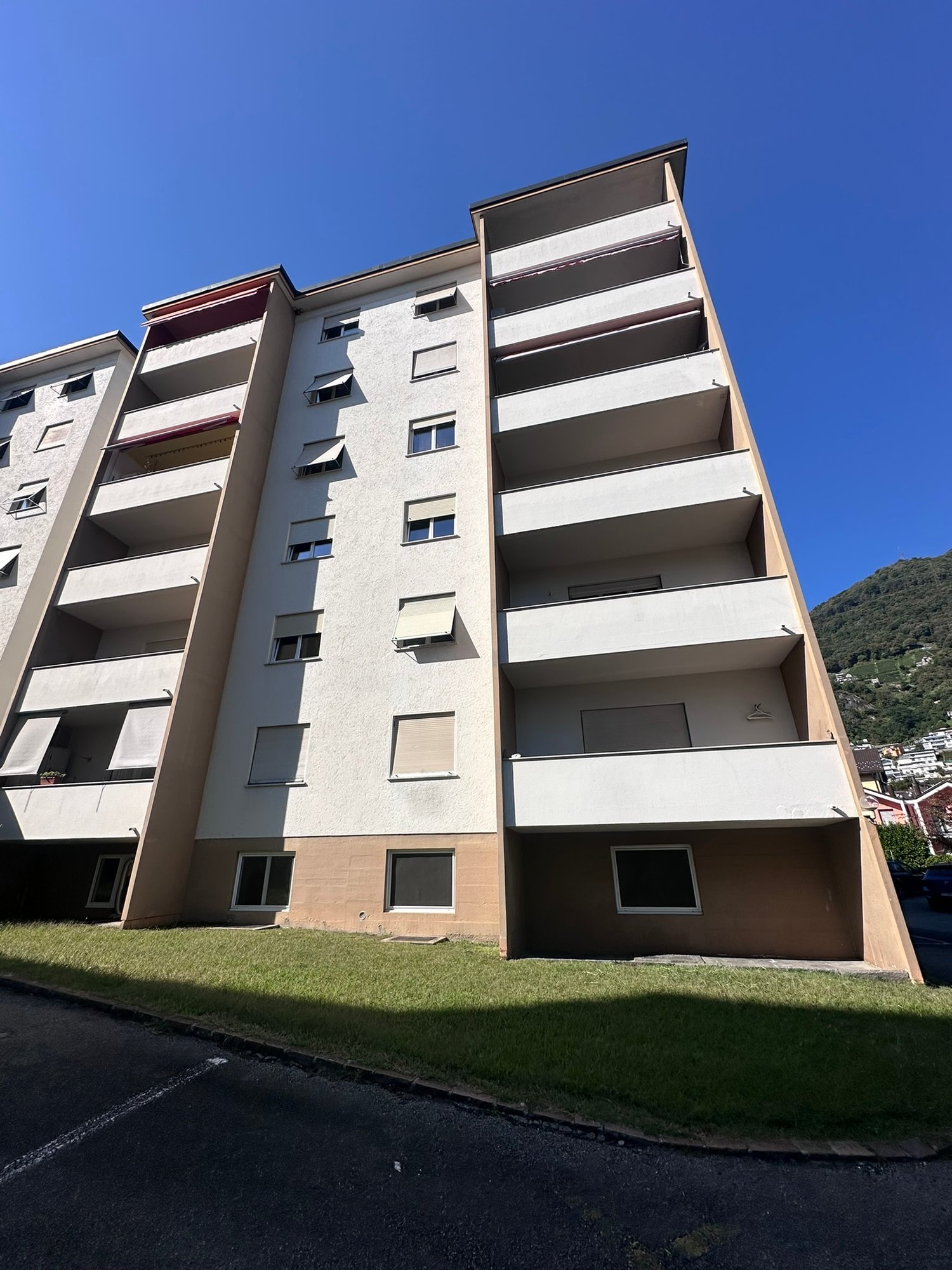 High-rise building, multiple floors, multiple balconies, greenery in front, parking area