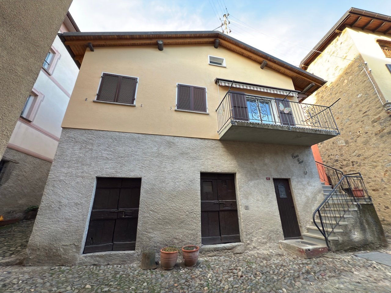 2 story house, stone facade, raised ground floor, balcony, two large wooden doors, stone steps