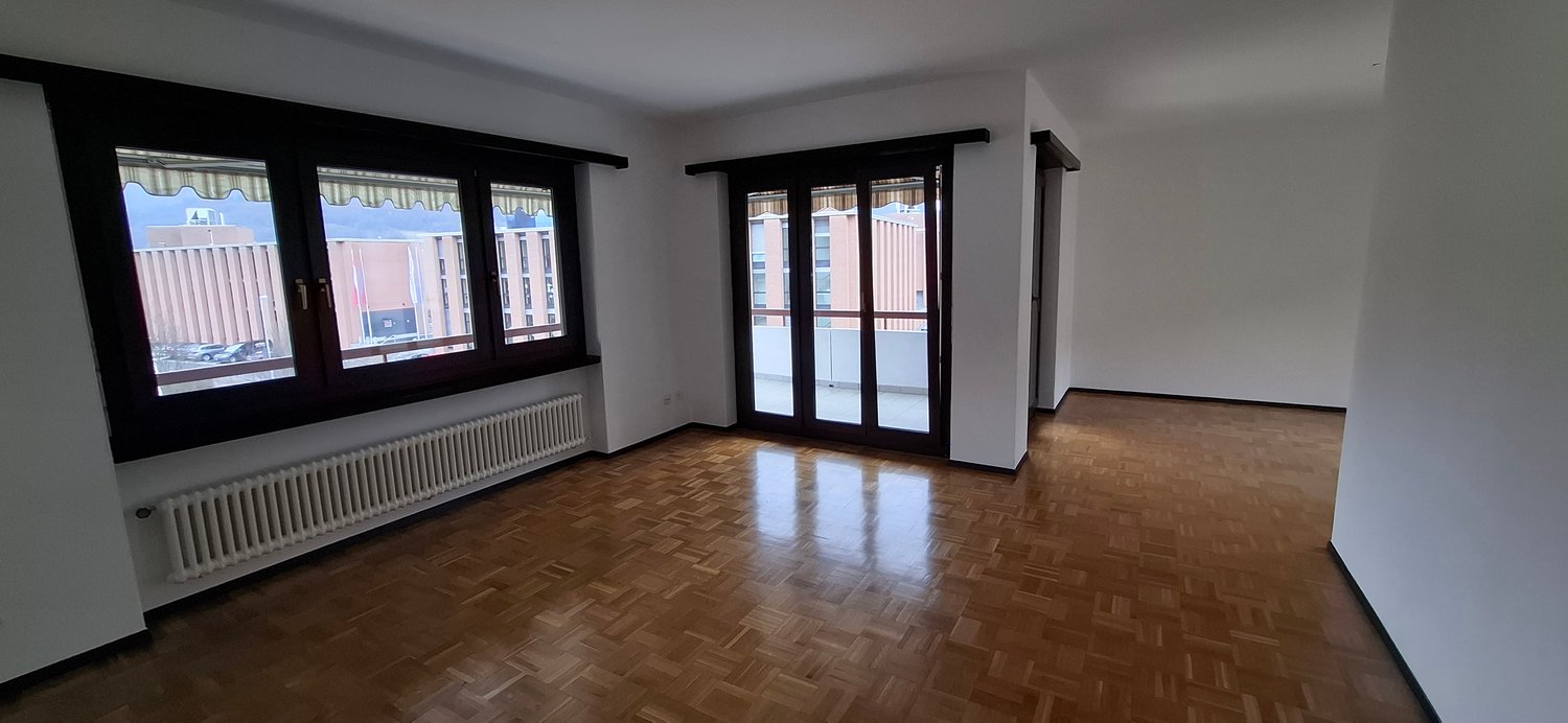 Empty room with wooden flooring, white walls, 2 windows, balcony, central heating radiator
