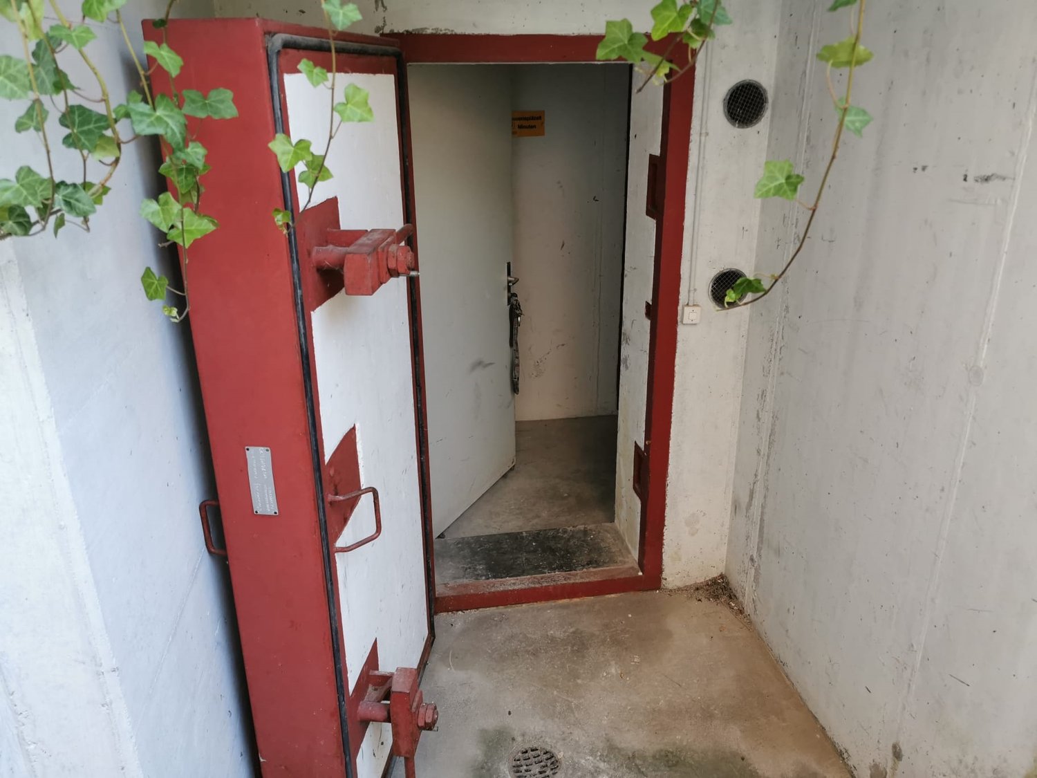 a small storage room with open door, cement floor, metal grate on the wall