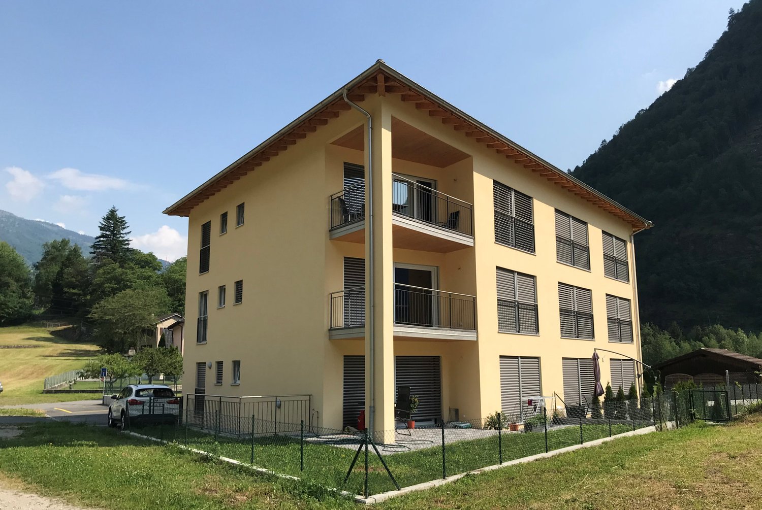 3-story yellow building, multiple balconies, private parking, green surroundings, fenced yard