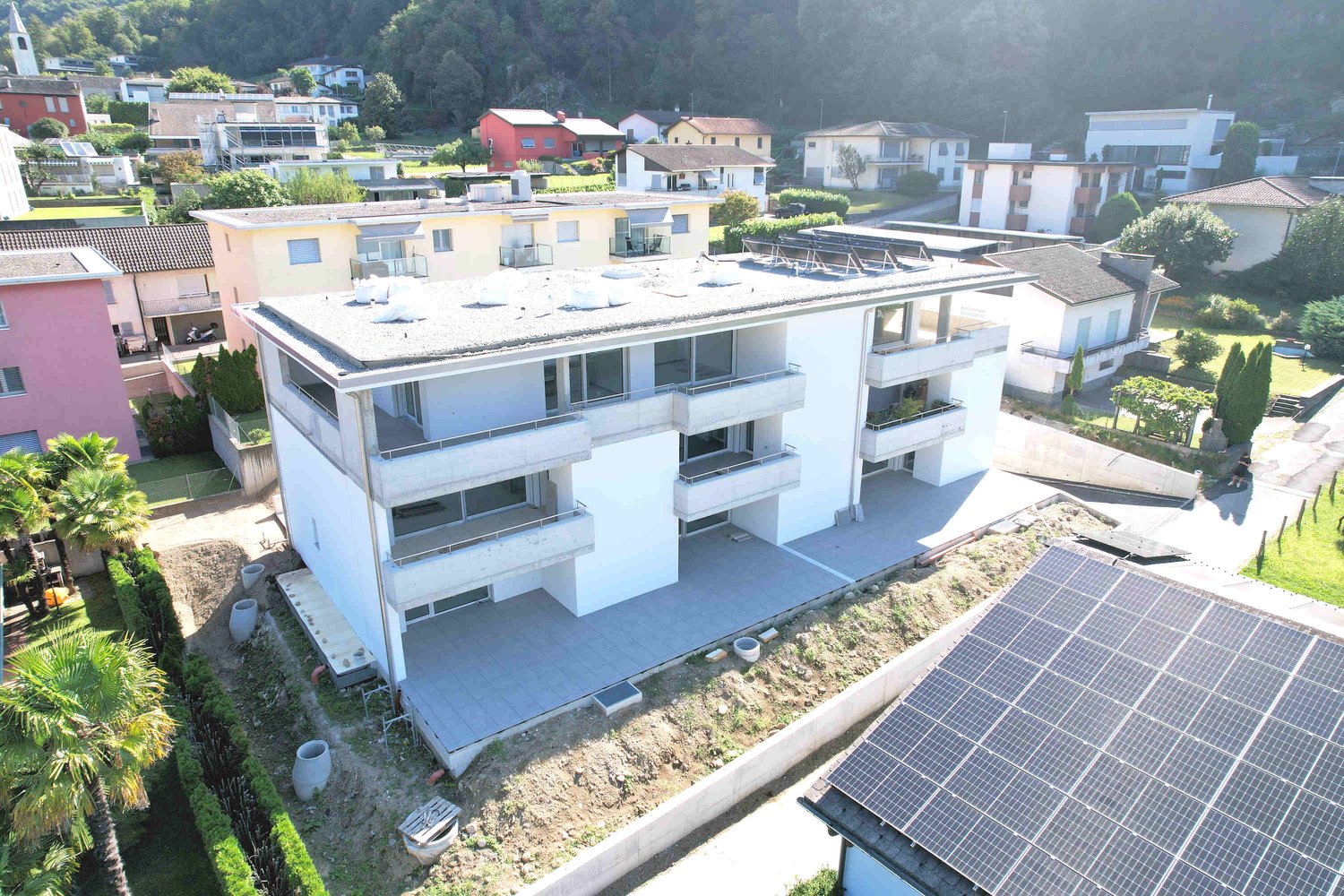 Multi-unit building with balconies and solar panels, situated in a neighborhood with diverse residential properties, some with mountain views
