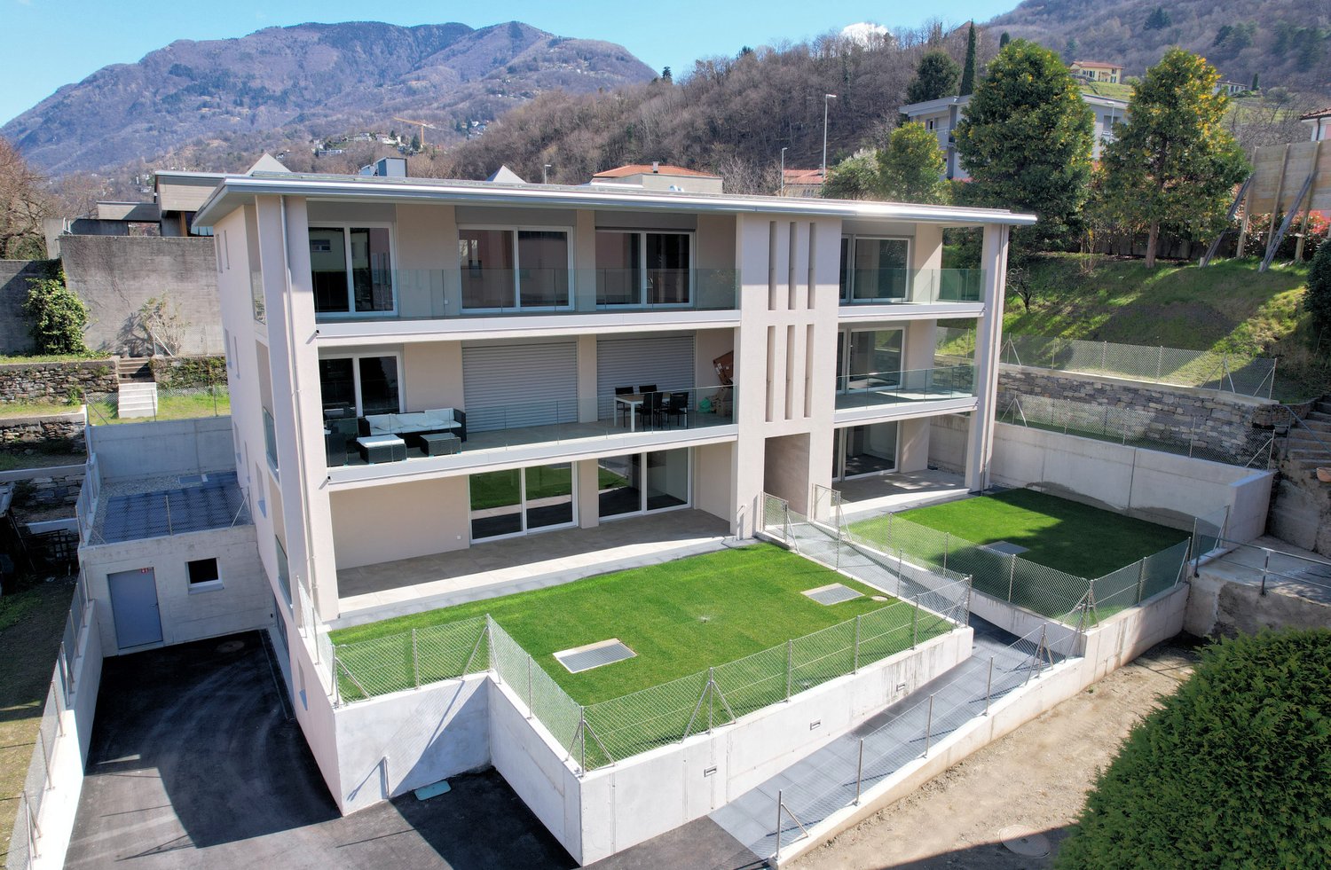 3 story house, white stucco, glass balconies, green grass lawn, parking area