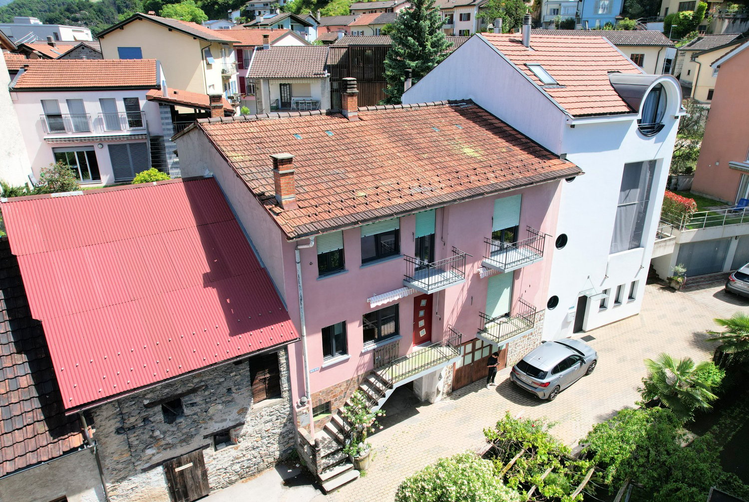 pink house with multiple balconies and red roof, two chimneys visible, large garden in front, street
