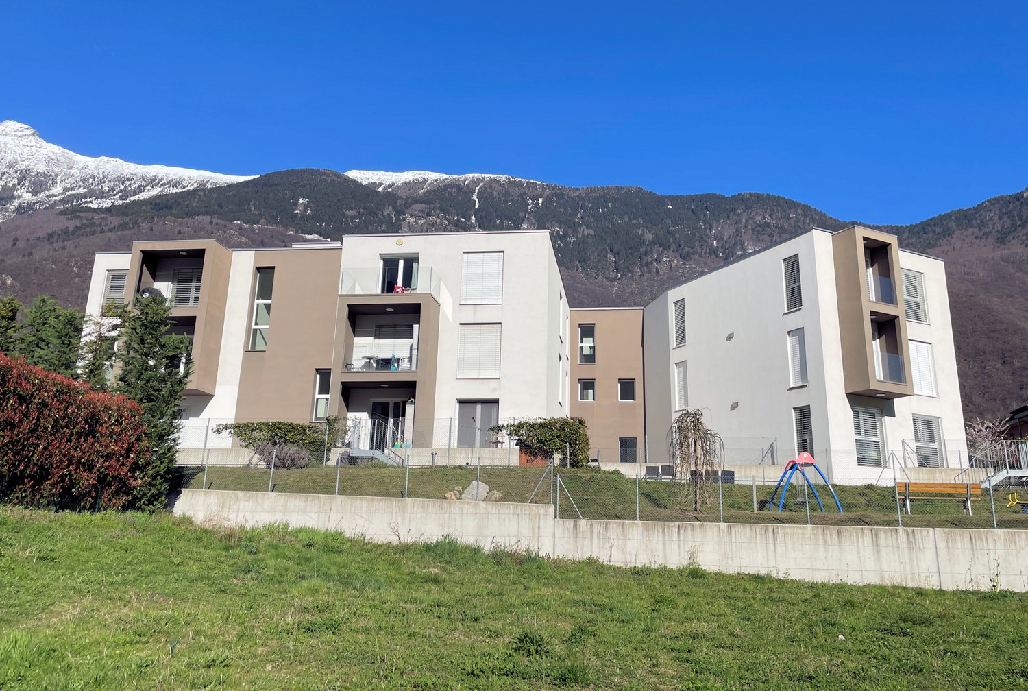 Modern apartment building with balconies, surrounded by greenery and mountains
