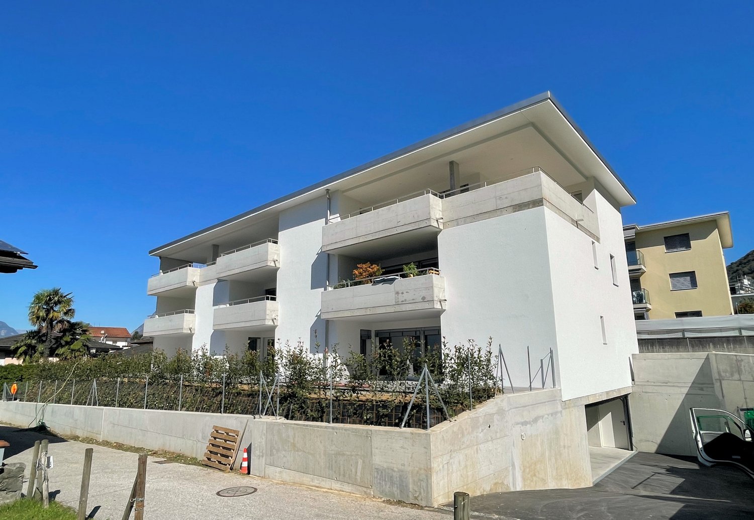 modern white building, multiple balconies, concrete wall, parking area