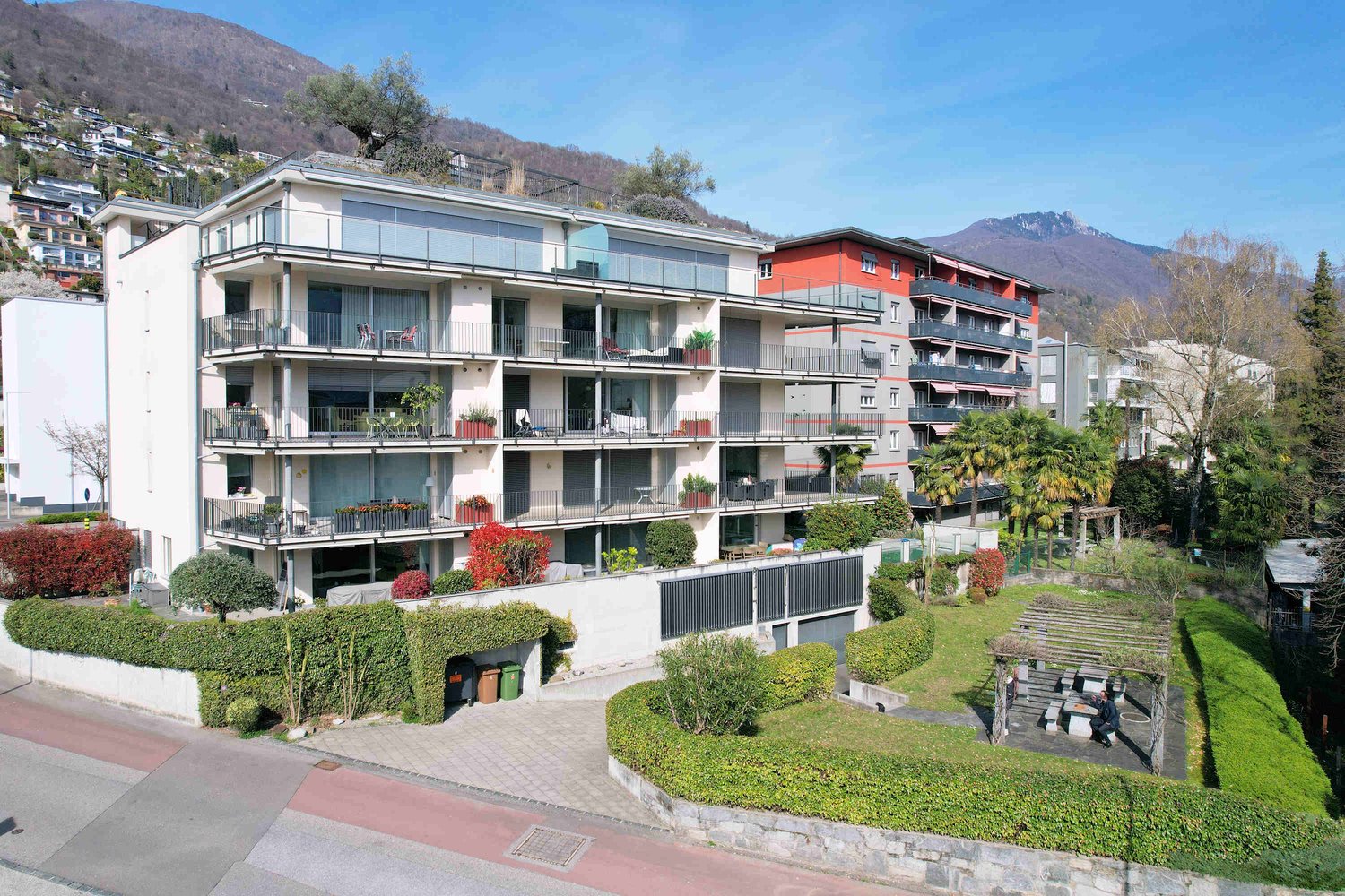 Modern apartment building with multiple balconies, surrounded by greenery and mountains in the background