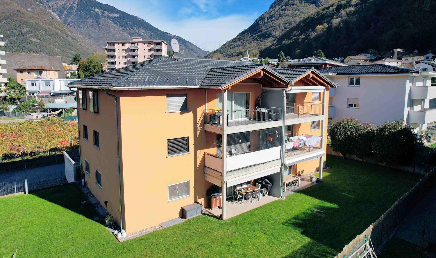 3 story house, yellow exterior, multiple balconies, green lawn, mountains in the background