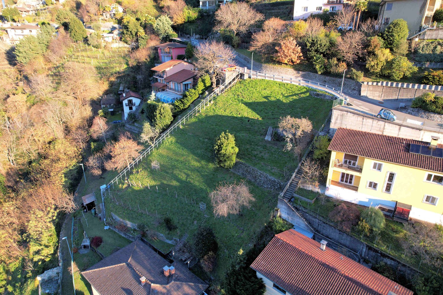 Aerial view of a residential area with several houses, a large grassy field, and a road.