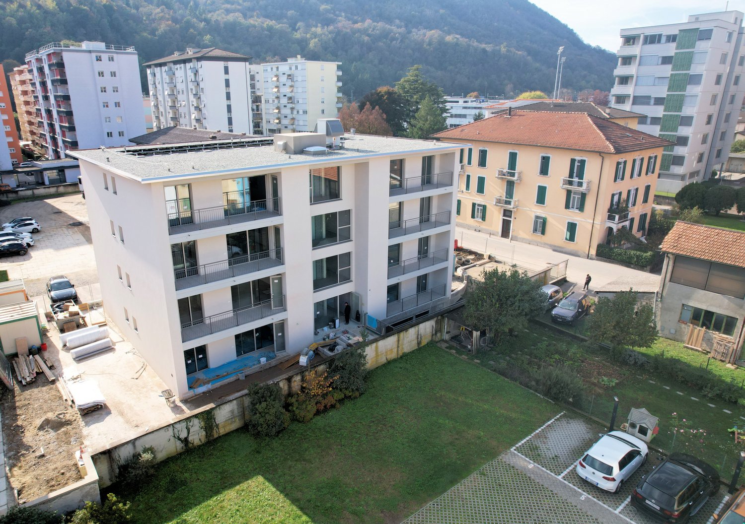 A multi-story building with multiple balconies, a parking lot, and a grassy area in front.