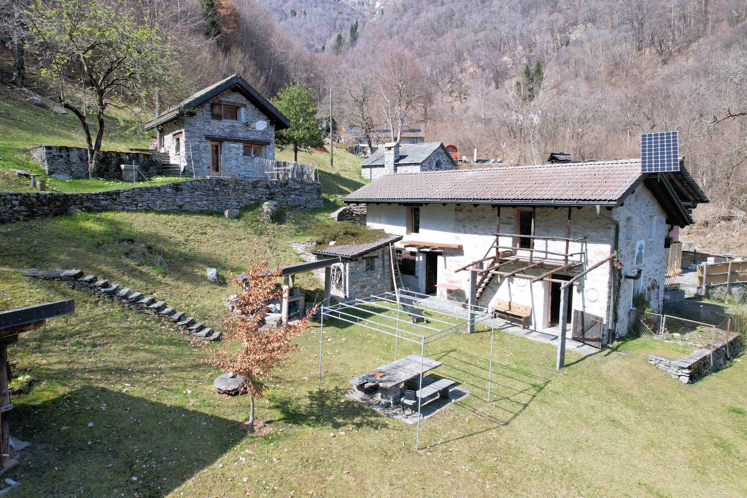 Stone house with solar panels, wooden benches, stone steps, and a metal structure with a table and benches