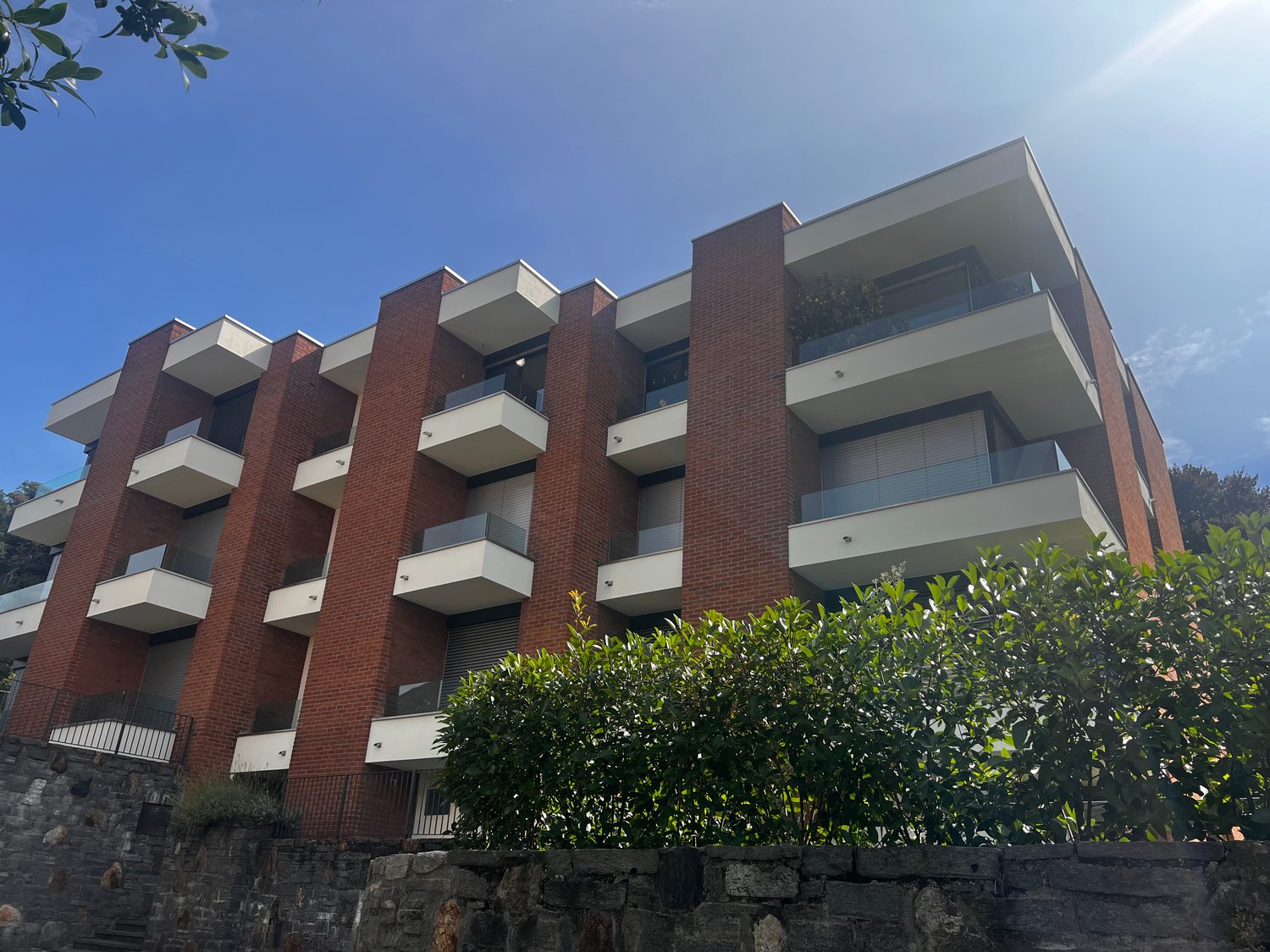 A modern brick apartment building with multiple balconies and a stone wall in front
