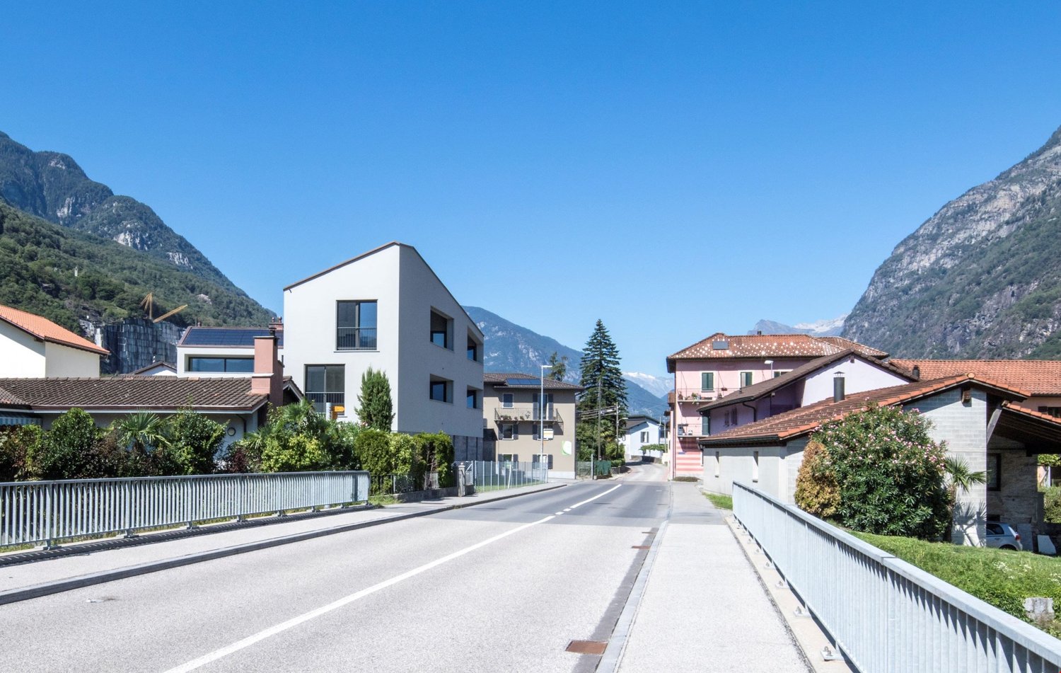 A quiet street with houses on both sides, a clear sky, and mountains in the background