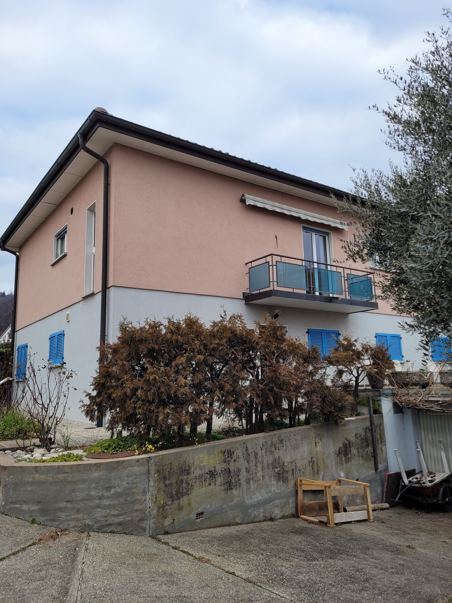 2-story residential building with a pink exterior, a balcony with glass railings, and trees surrounding the property.