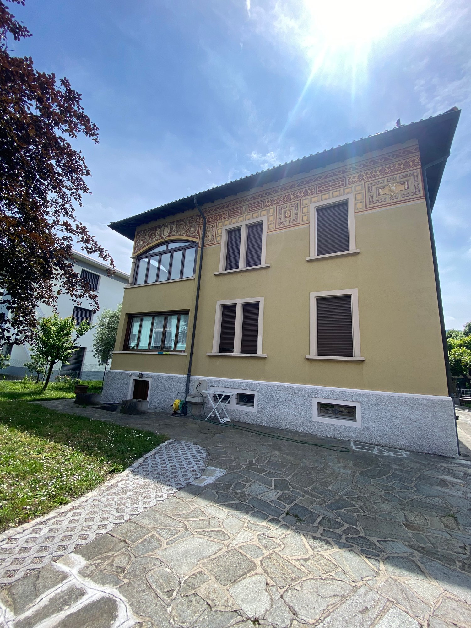 2-story building with ornate facade, yellow walls, decorative trim, large windows, stone pathway leading to the entrance