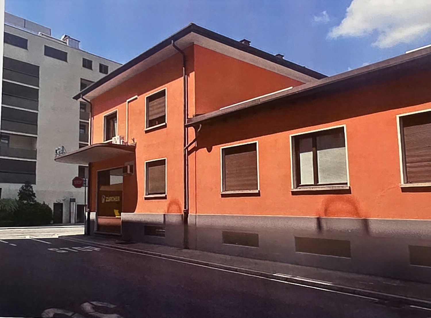 2-story orange building with large windows, located on a street with other buildings in the background