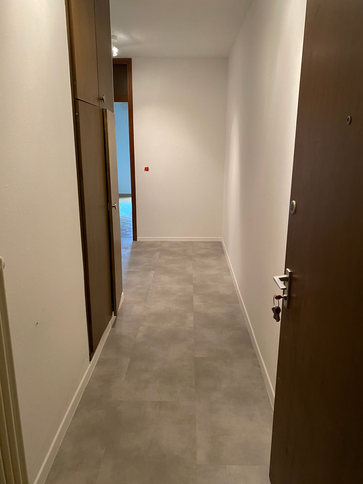 Empty hallway with two doors, tiled floor, white walls, ceiling lights