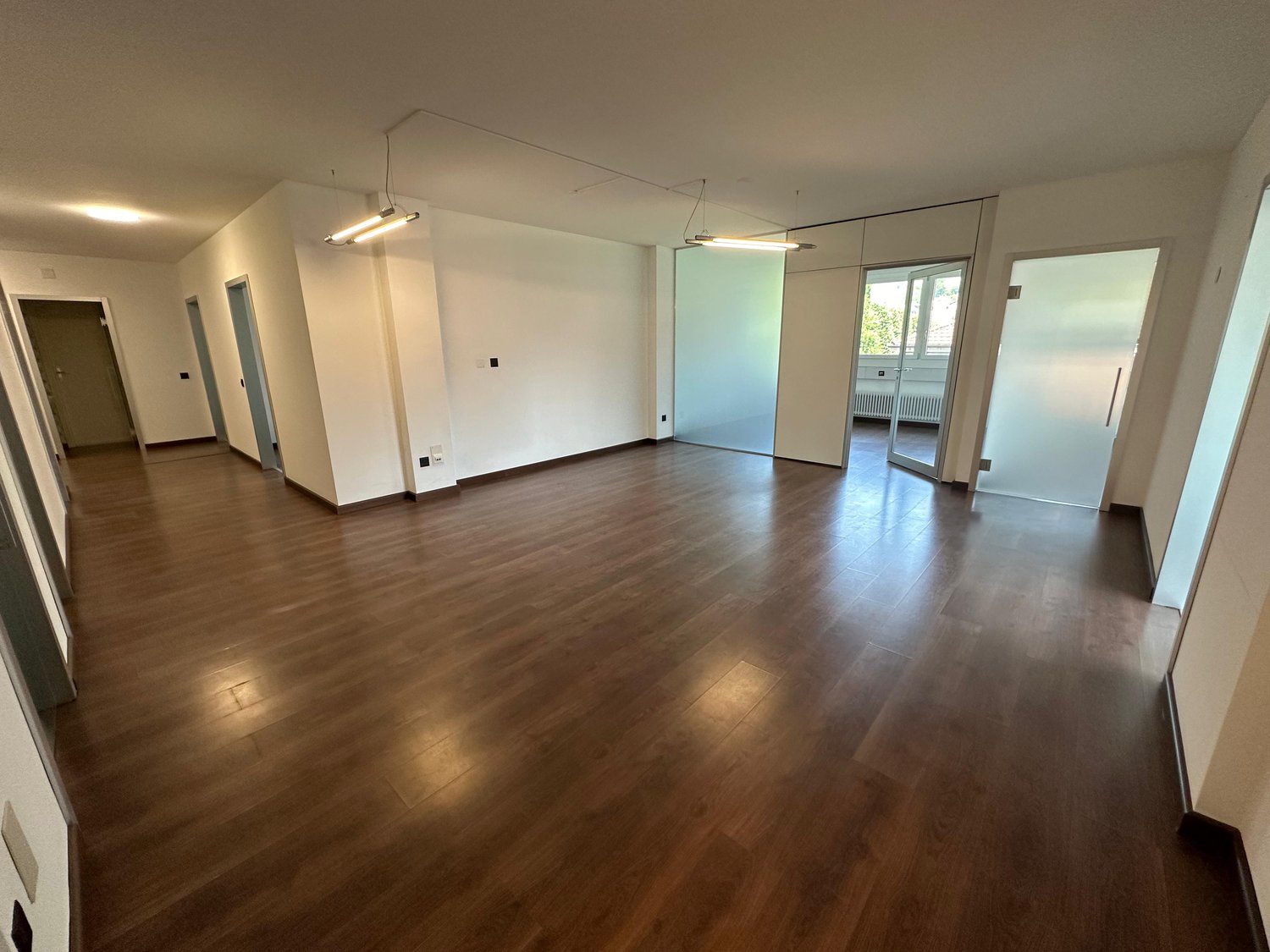 Empty room with wooden floors, white walls, and glass doors leading to another room.