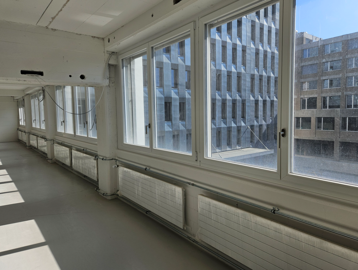 Empty office room with large windows, radiators, grey flooring