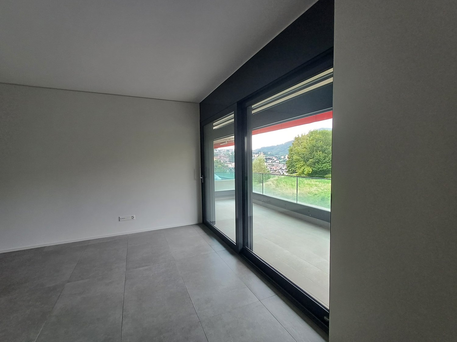 Spacious room with large windows offering a scenic view, grey tiled flooring, and dark-colored walls.