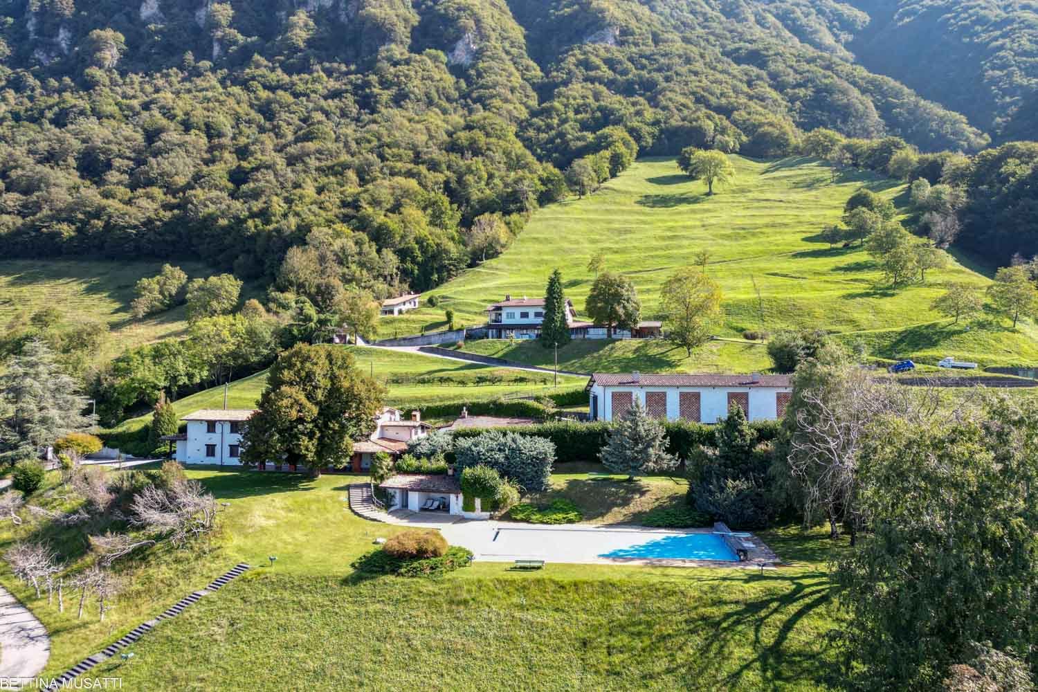 House on a hillside, swimming pool, beautiful views, large green field, lush greenery, several houses
