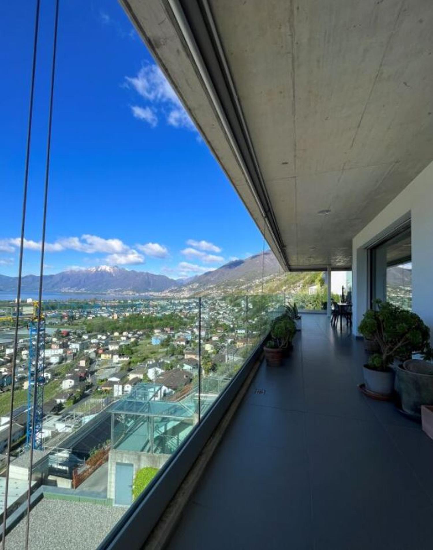 Terrace with glass railings, view of city and mountains, table, chairs, plants, and trees