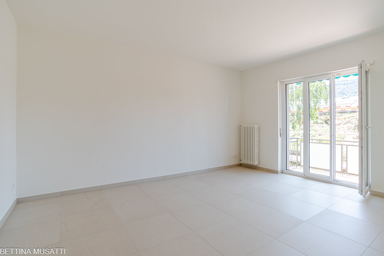 Empty room with white walls and tiled floor, sliding glass doors leading to a balcony