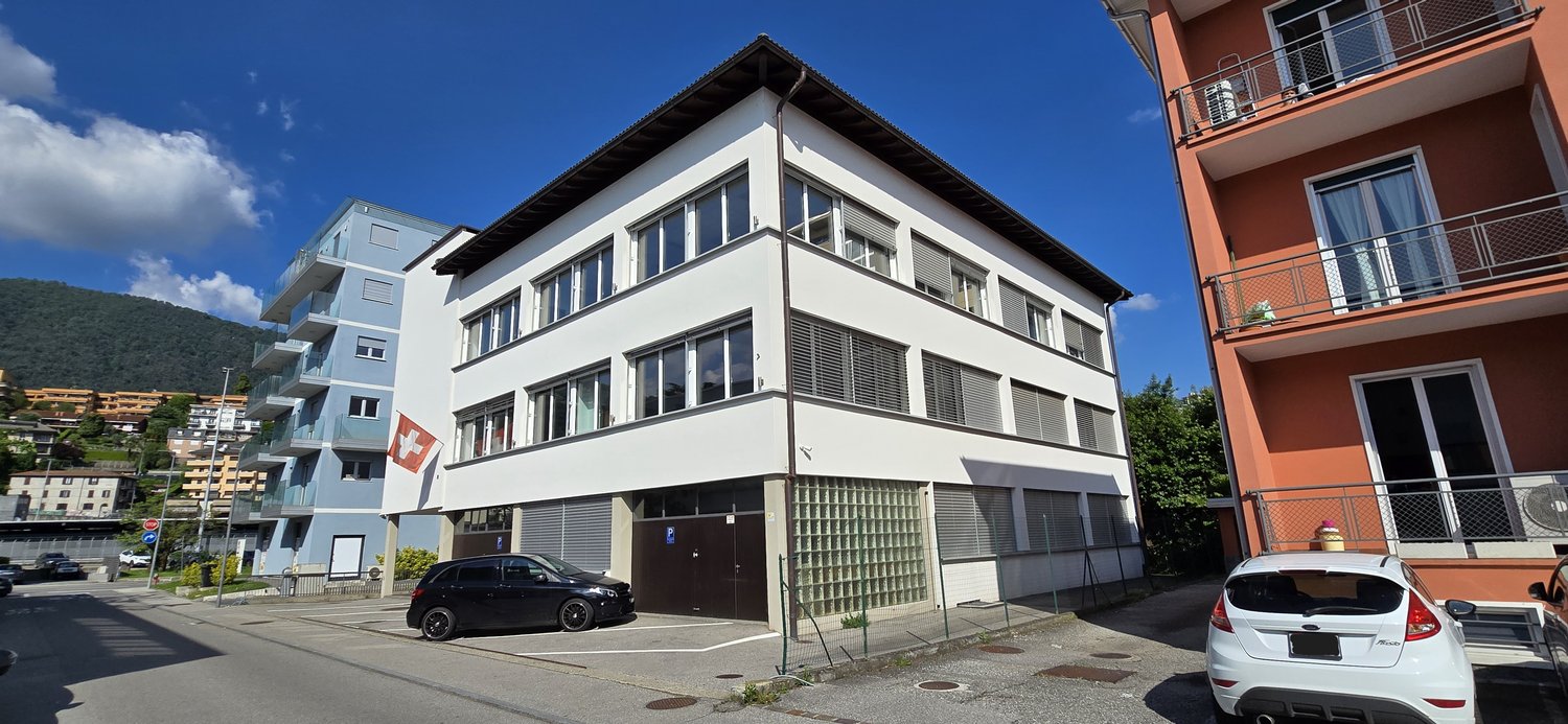 Three-story building, white exterior, garage, red Swiss flag on the wall