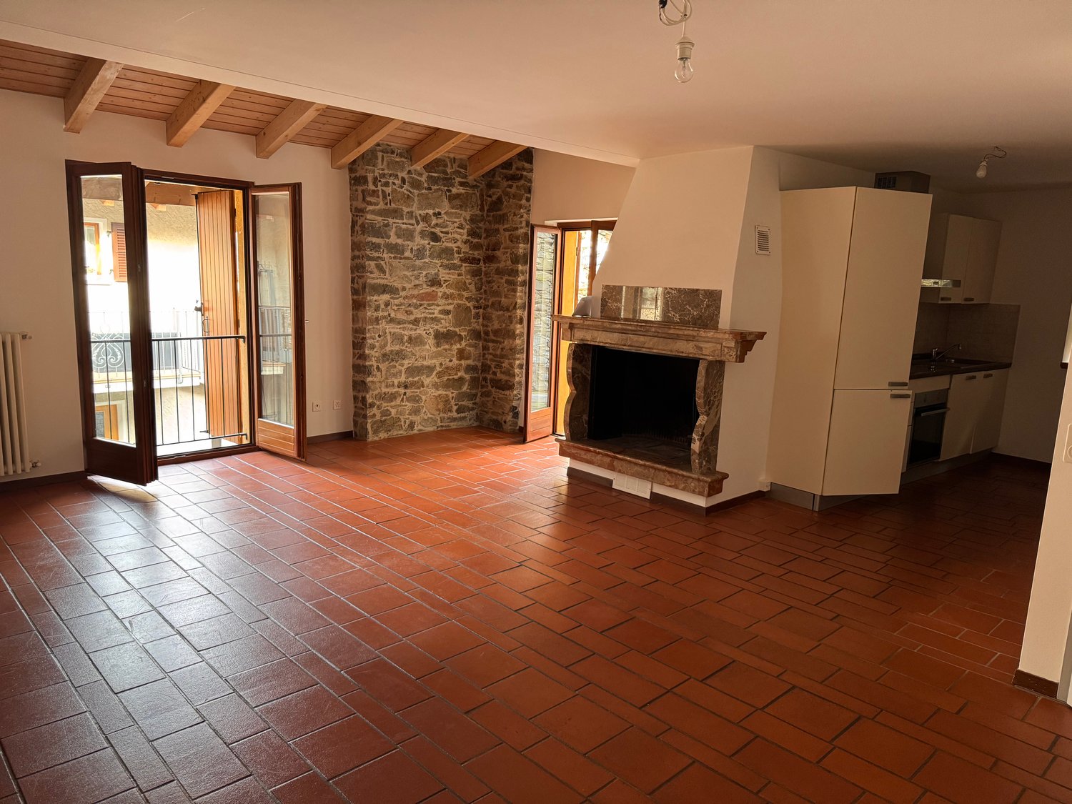 Open layout, fireplace, stone wall, red tile floor, large windows, balcony
