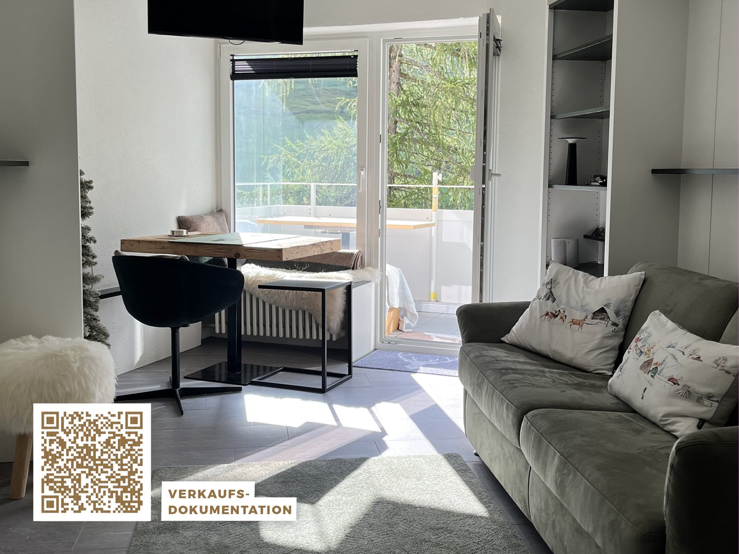 gray couch, 2 pillows, dining table with 2 chairs, TV, glass door leading to balcony, radiator, floor radiator