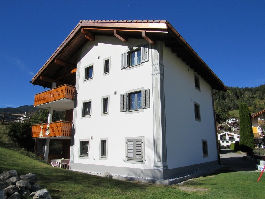 2 story house, white wall, brown roof, balcony, several windows, mountains in the background