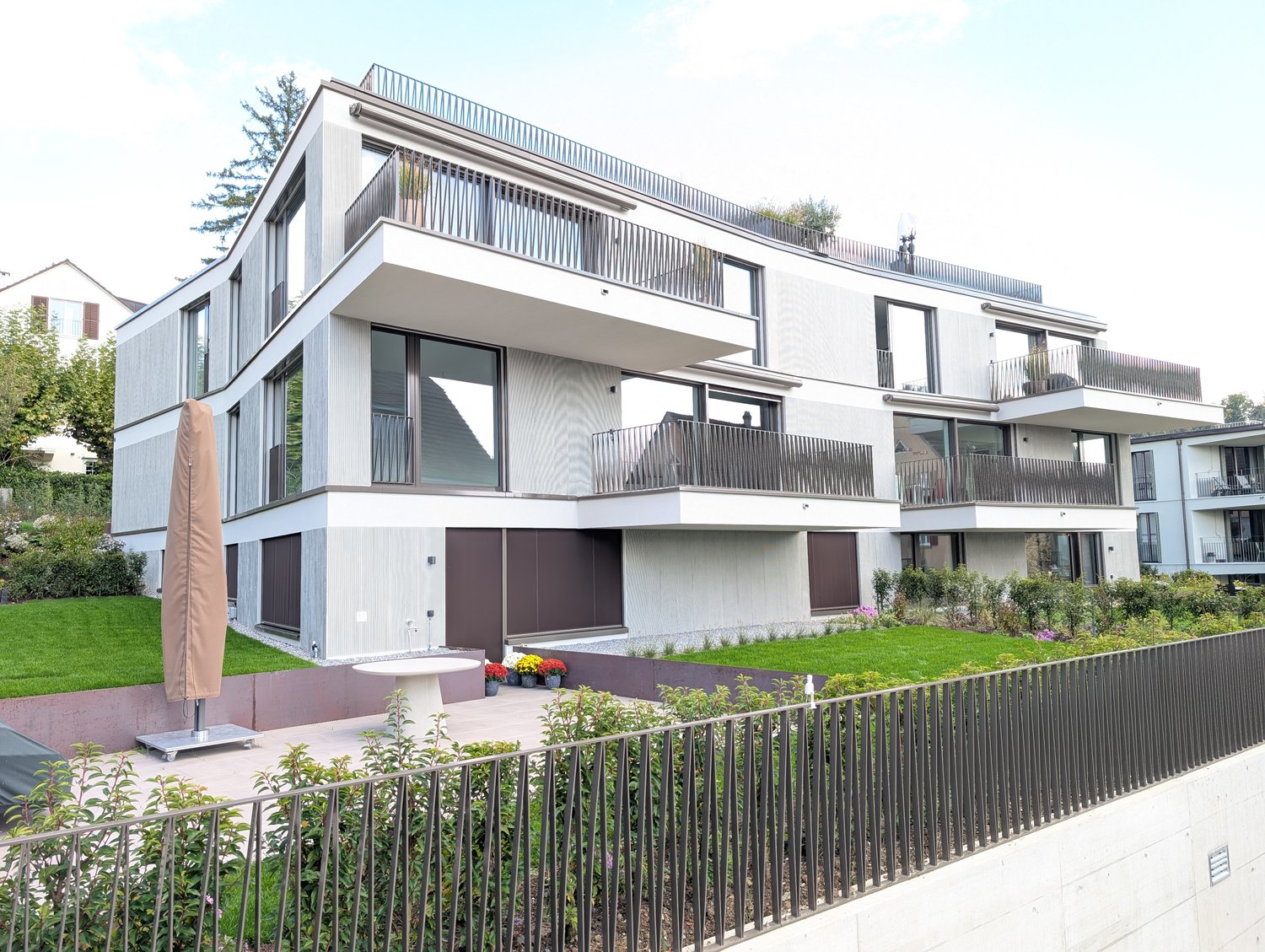 Modern three-story house, white exterior, multiple balconies, landscaped garden, metal railings, brown entry doors