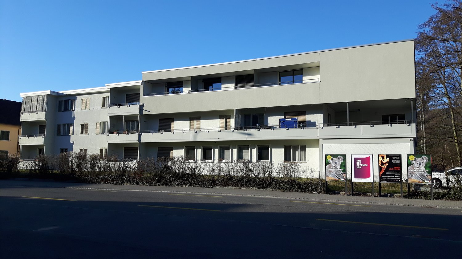 White 3 story building with several balconies, windows, concrete foundation
