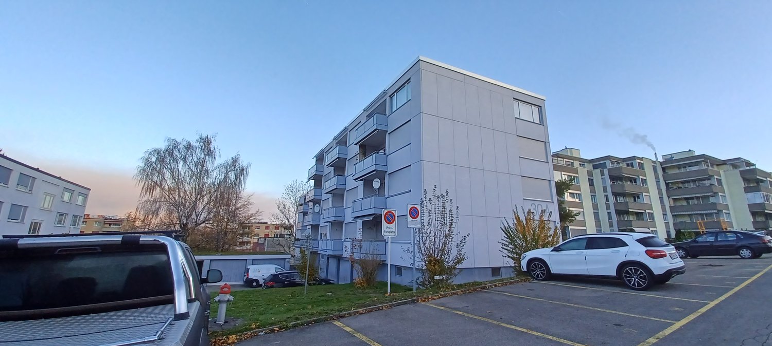 large building with many balconies, white walls, multiple floors, and parking lot in front