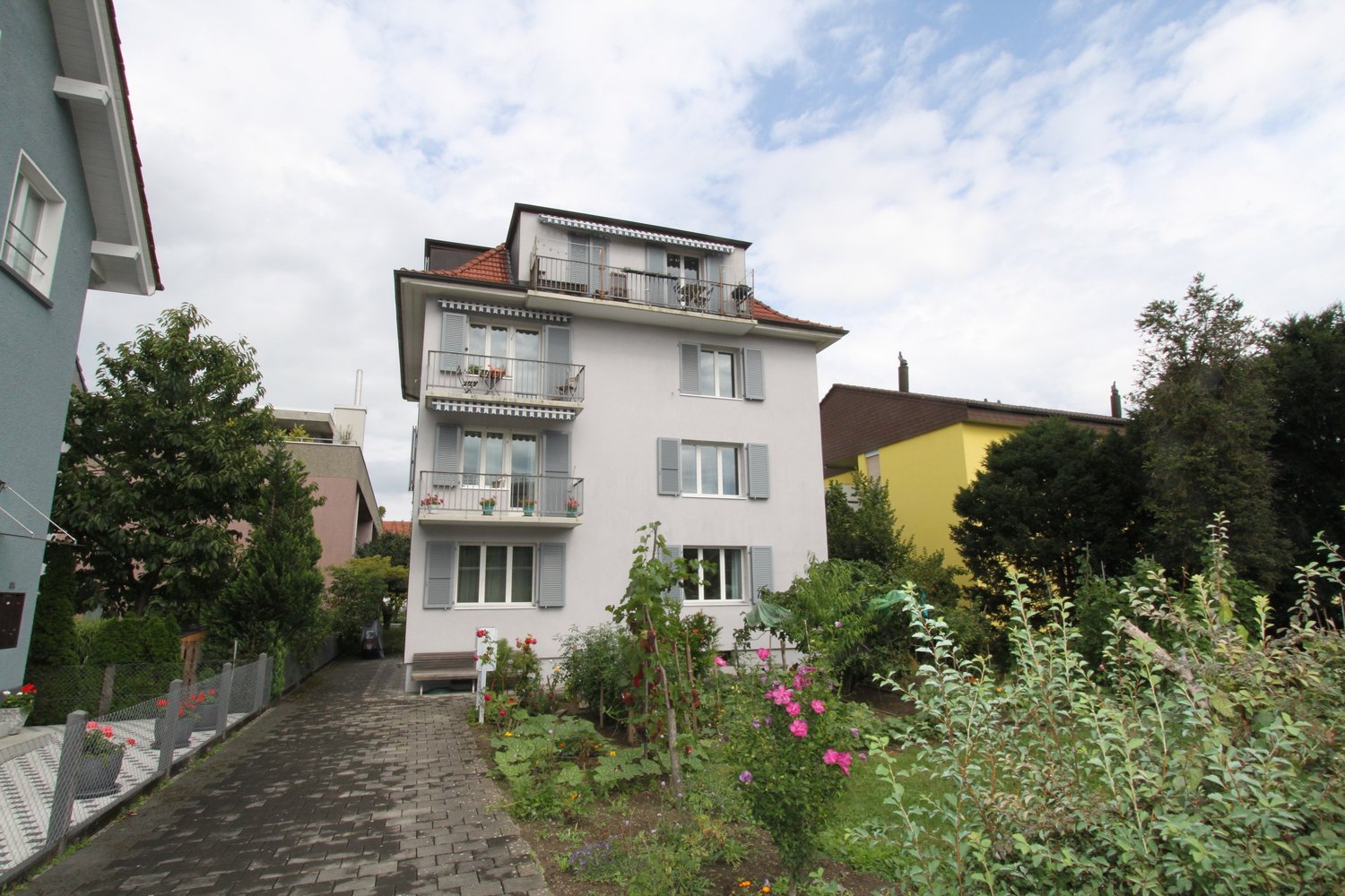 3-story house, white exterior, brown roof, balconies on 2nd and 3rd floors, brick path leading to front entrance